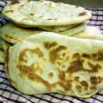 Homemade naan flatbread stacked on a red and white kitchen towel.