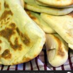 Homemade naan flatbread stacked on a red and white kitchen towel.