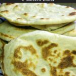 Homemade naan flatbread stacked on a red and white kitchen towel.