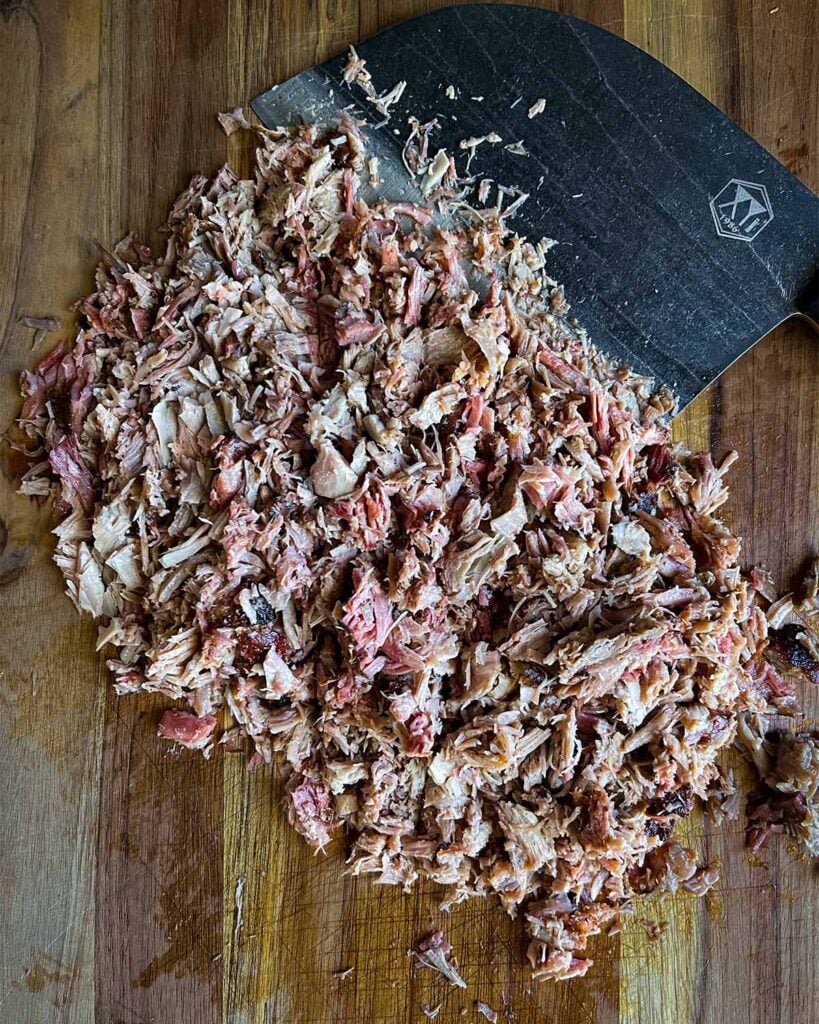 Pork butt, chopped, on a wooden cutting board with a large knife.