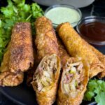 Redneck egg rolls on a dark plate. One is cut in half and standing up.