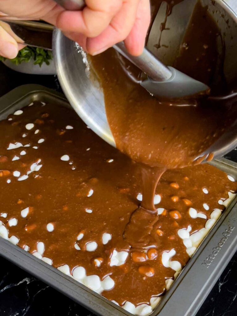 Chocolate frosting being poured over the melted mini marshmallows on the Mississippi Mud Cake.