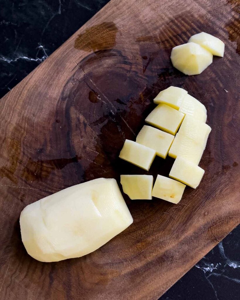 Russet potato diced on a wooden cutting board.