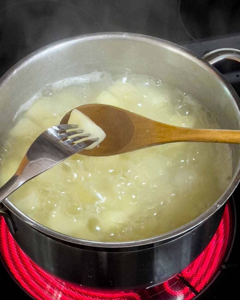 A fork is inserted into a boiled potato over the boiling pot.