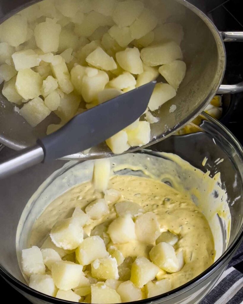 Boiled potatoes being added into the Southern potato salad dressing.