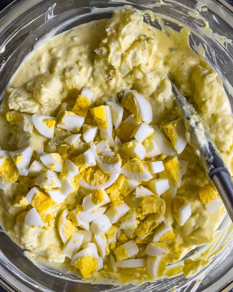 Chopped hard-boiled eggs added to the Southern potato salad in a glass mixing bowl.