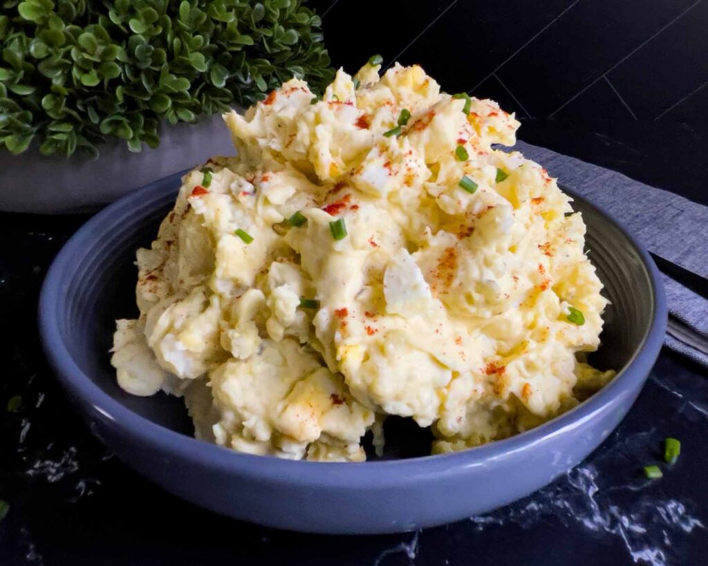 Southern potato salad in a bowl garnished with chives and paprika.