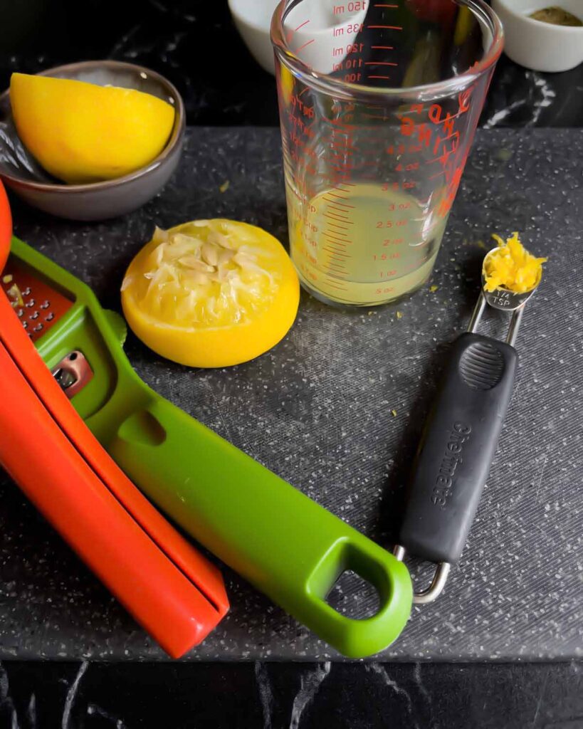 Juiced lemon and lemon zest for whipped feta on a dark cutting board.