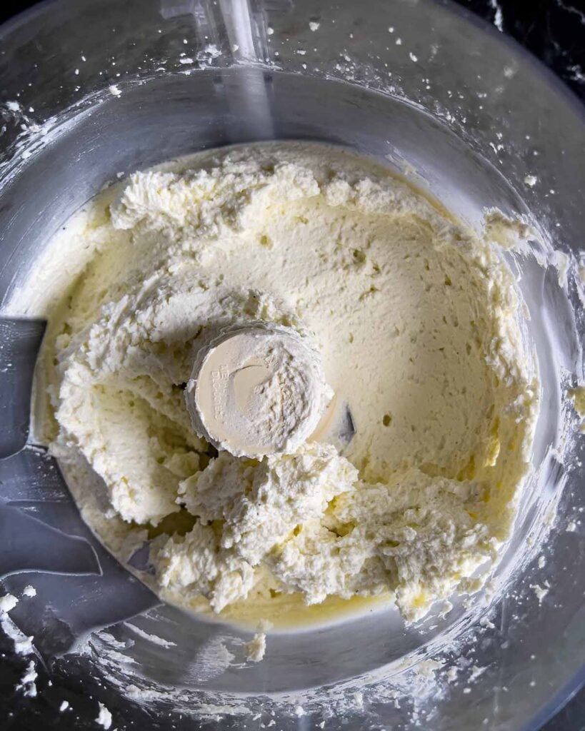 Whipped feta partially mixed in the bowl of a food processor.