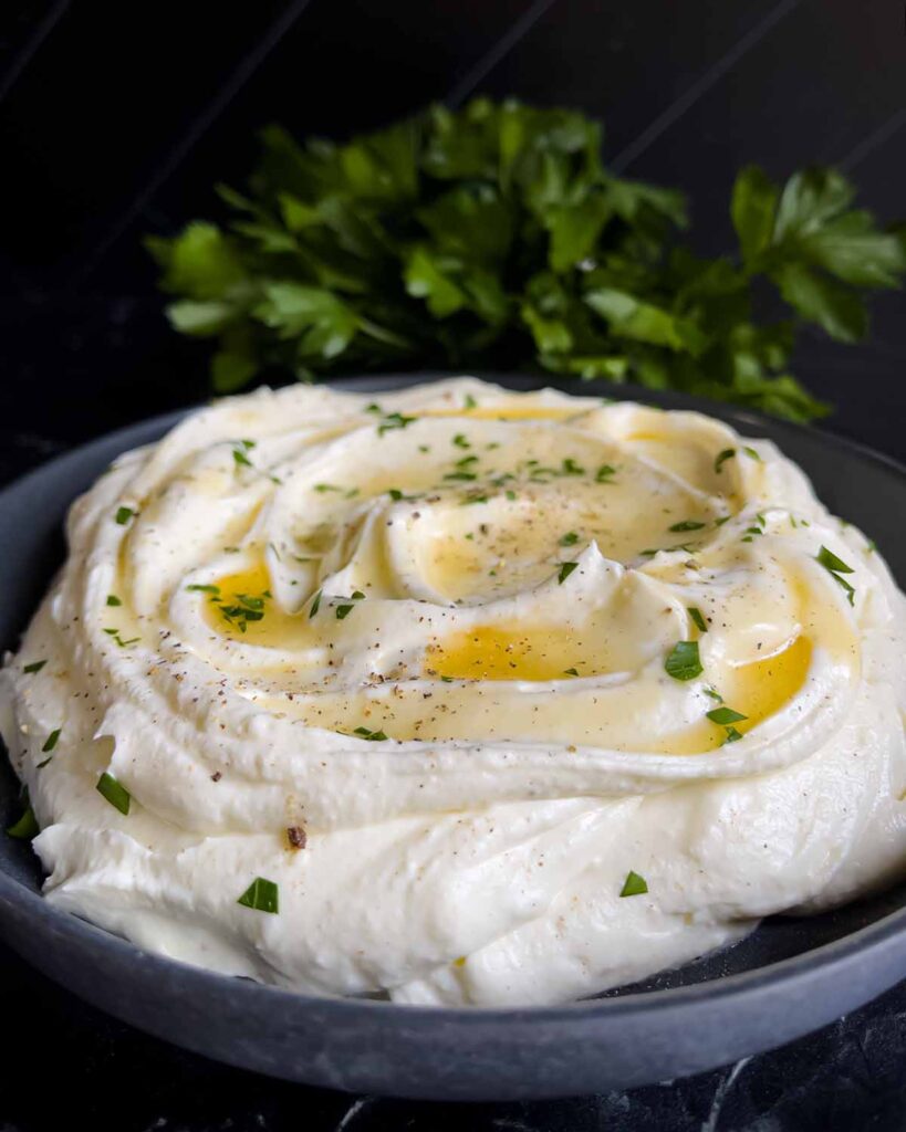 Whipped feta garnished with honey, chopped parsley, and black pepper in a dark bowl.