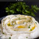 Whipped feta garnished with honey, chopped parsley, and black pepper in a dark bowl surrounded by pita chips and pita bread.