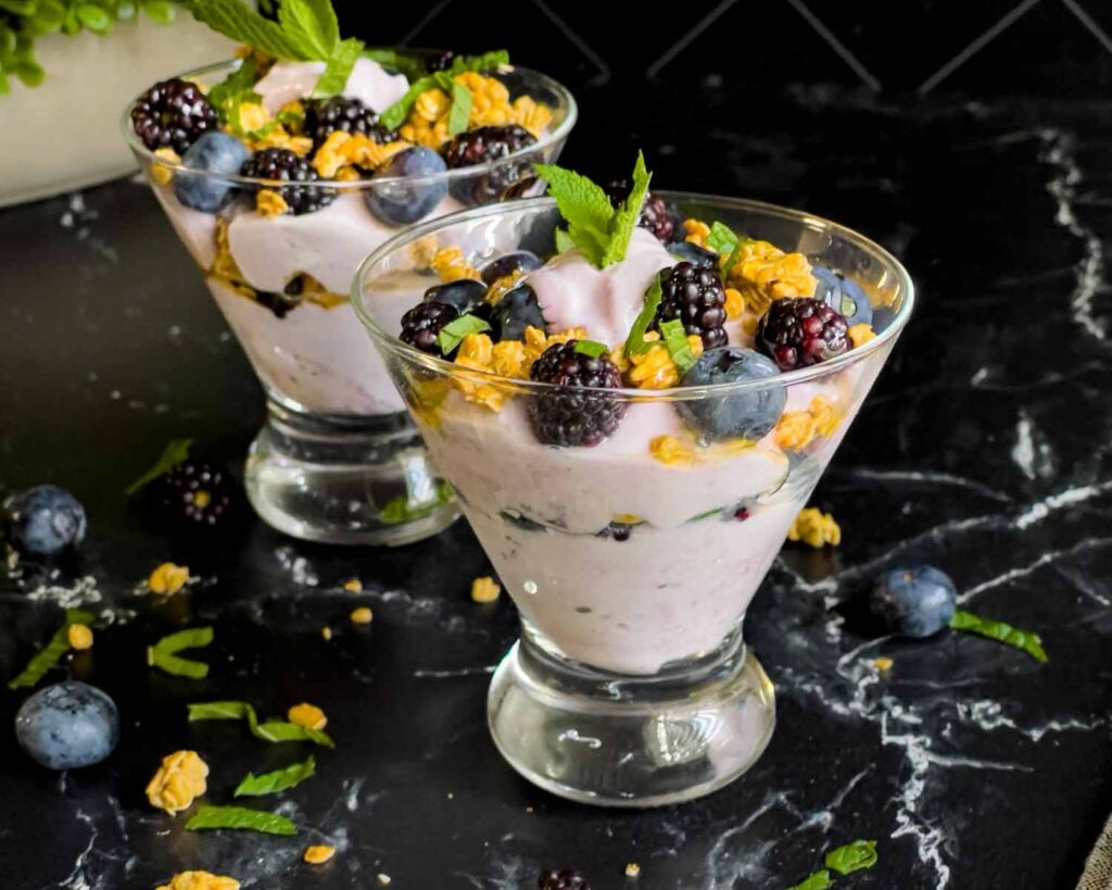 Berry yogurt parfait in a stemless martini glass on a dark surface.