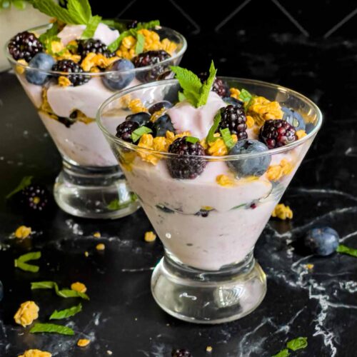 Berry yogurt parfait in a stemless martini glass on a dark surface.