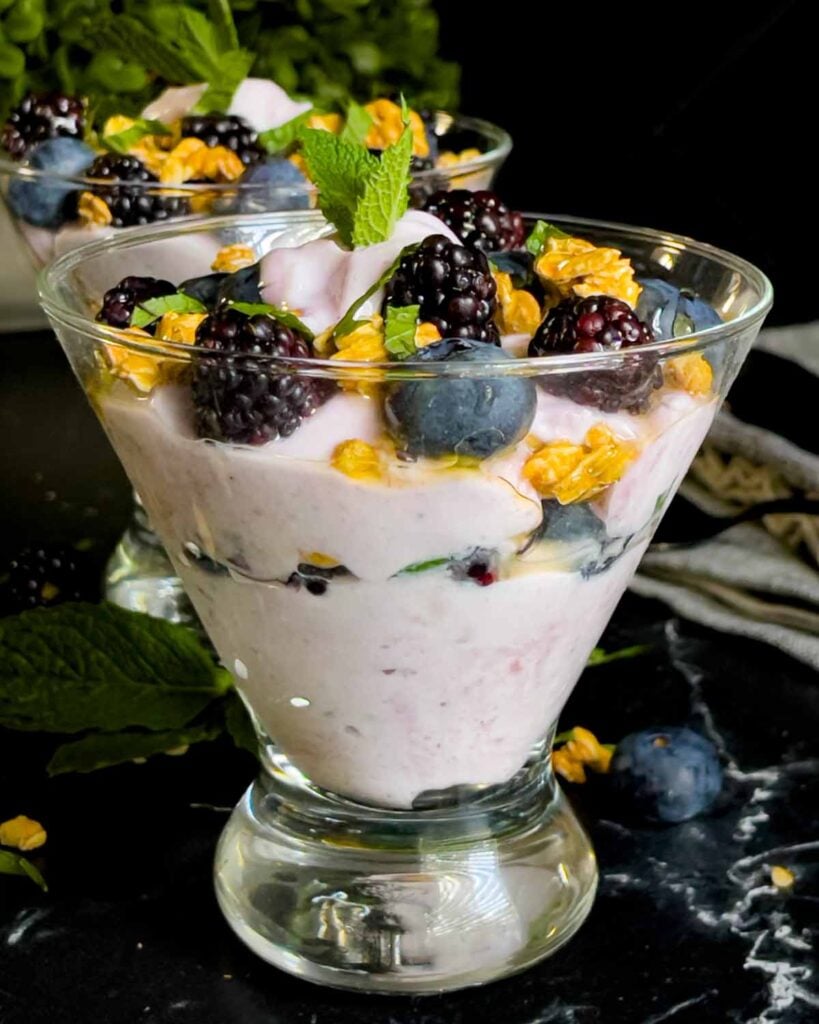 Berry yogurt parfait in a stemless martini glass on a dark surface.
