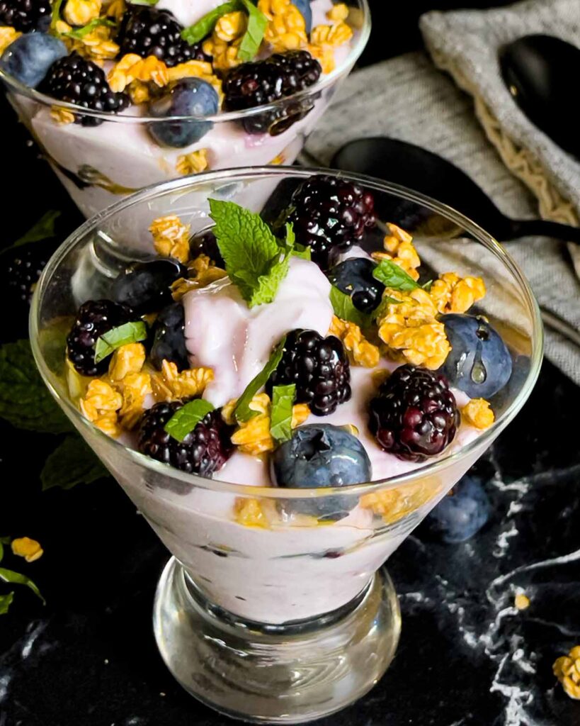 Berry yogurt parfait in a stemless martini glass on a dark surface.