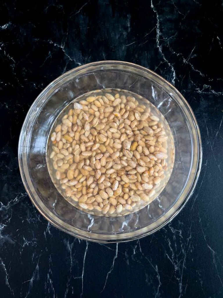 Pinto beans soaking in water in a glass bowl.