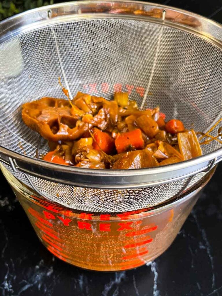 Straining the vegetables that cooked in the braising liquid of the beef cheeks.