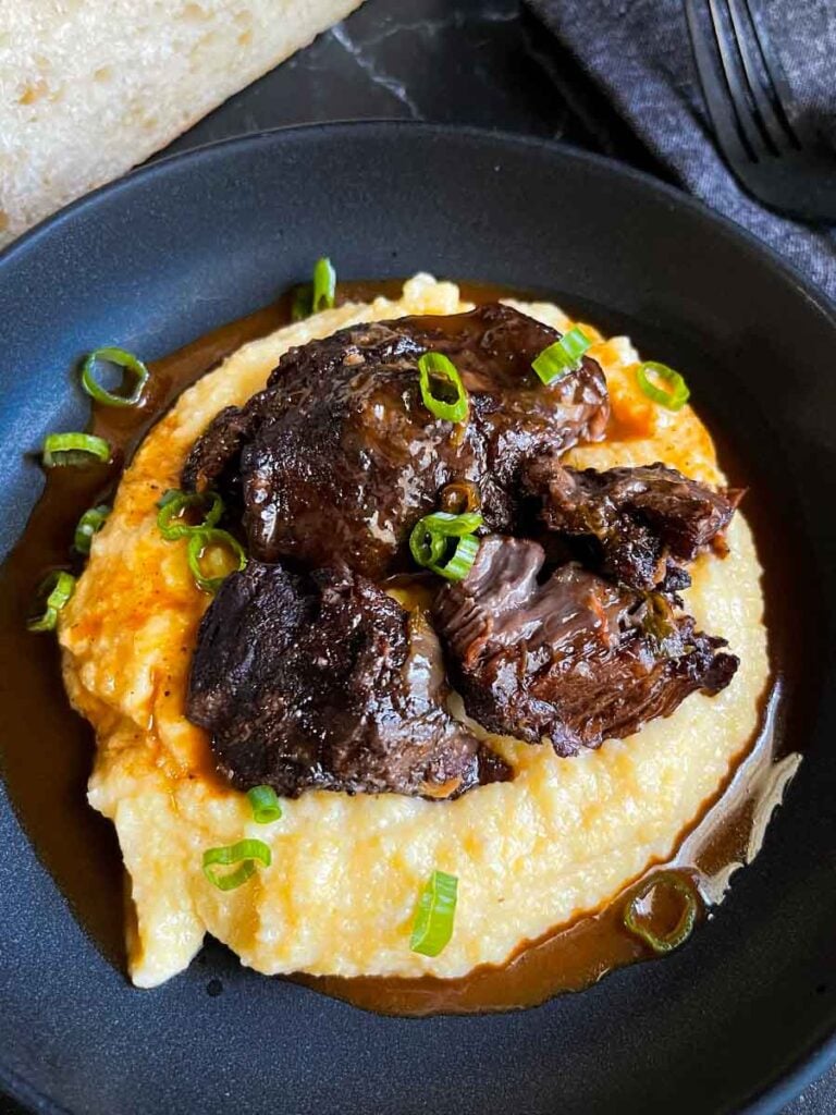 Braised beef cheek on a bed of polenta, garnished with green onion.