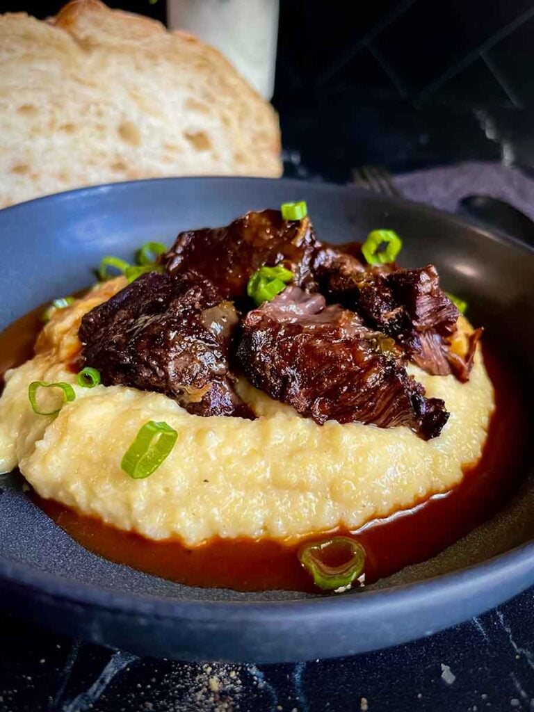 Braised beef cheek on a bed of polenta, garnished with green onion.