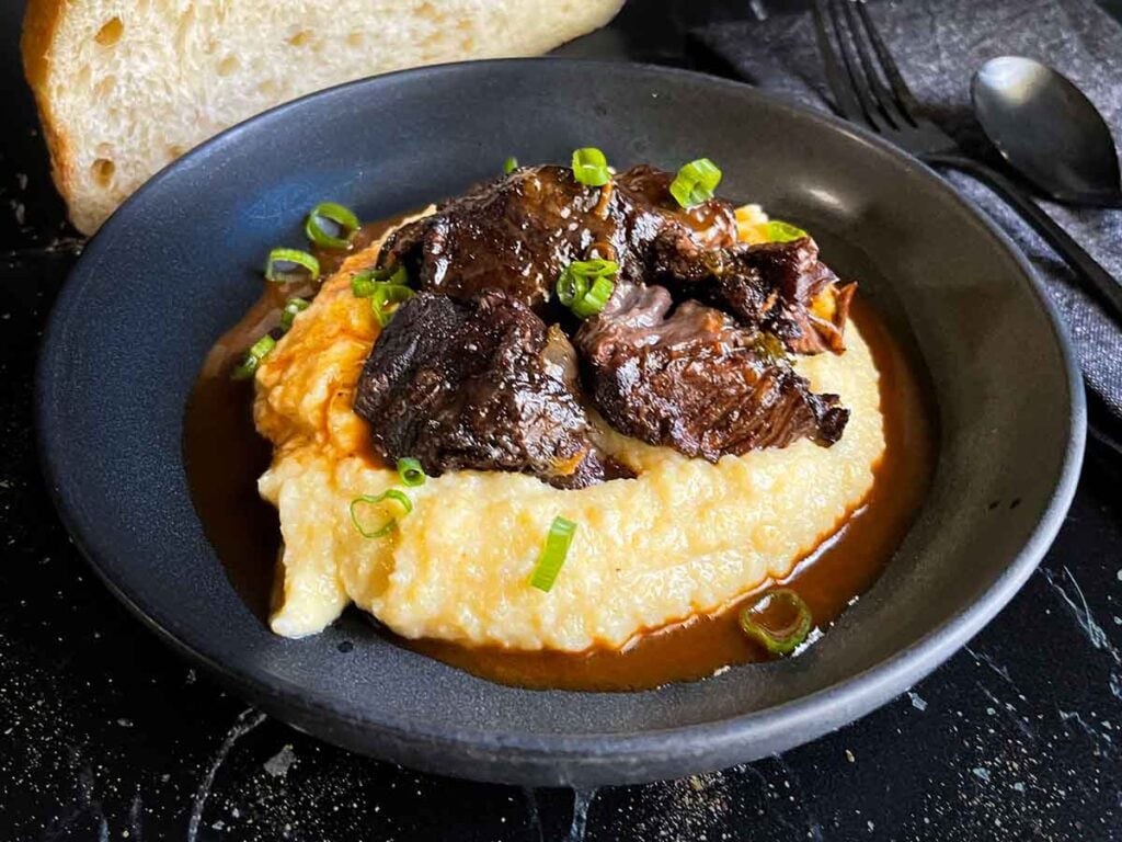 Braised beef cheek on a bed of polenta, garnished with green onion.