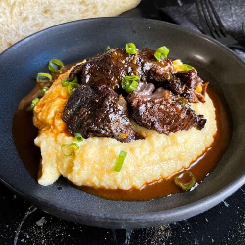 Braised beef cheek on a bed of polenta, garnished with green onion.