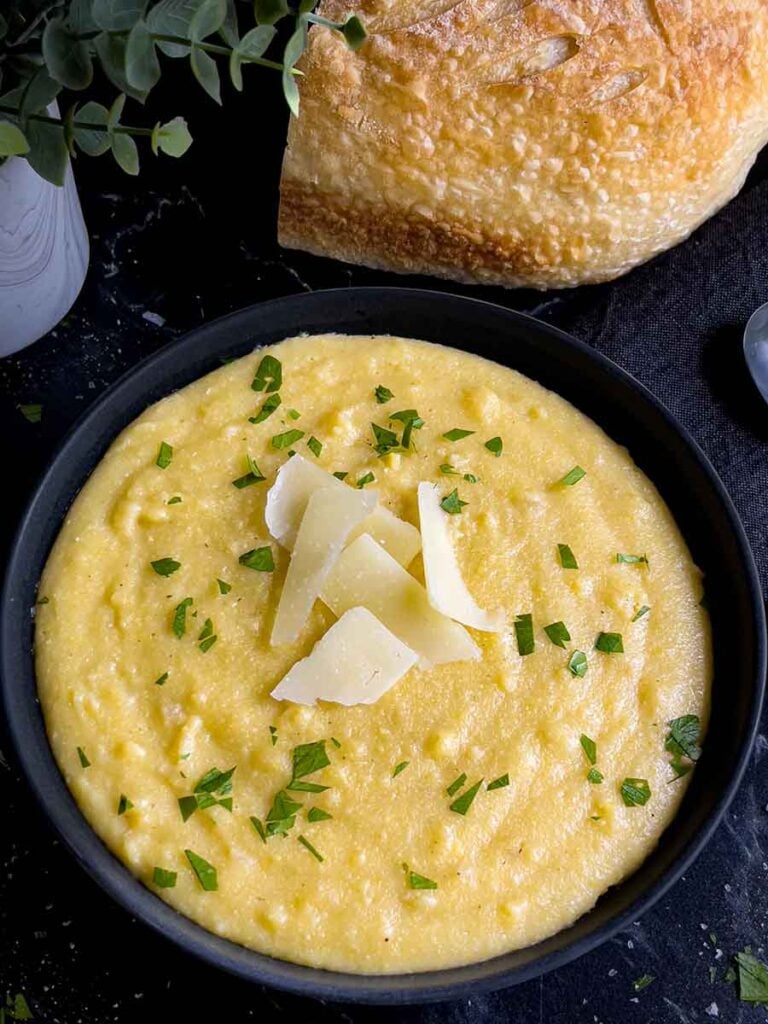 Polenta in a dark bowl garnished with chopped parsley and parmesan cheese.