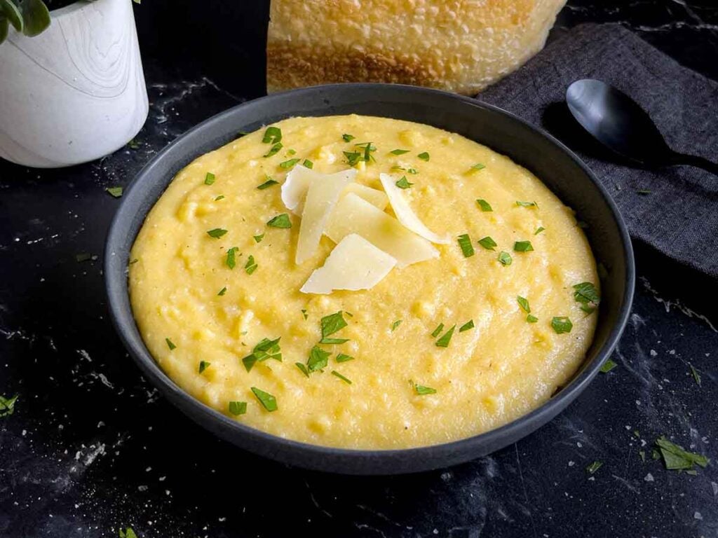 Polenta in a dark bowl garnished with chopped parsley and parmesan cheese.