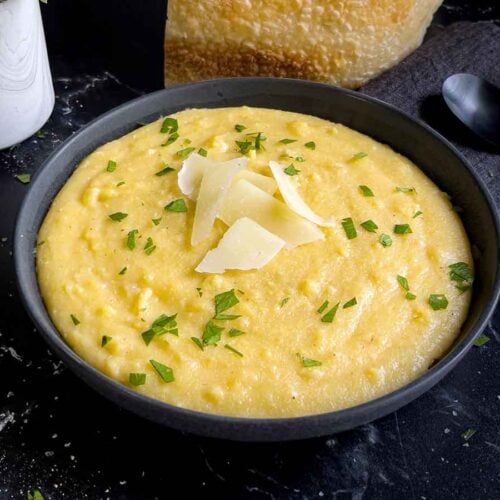 Polenta in a dark bowl garnished with chopped parsley and parmesan cheese.