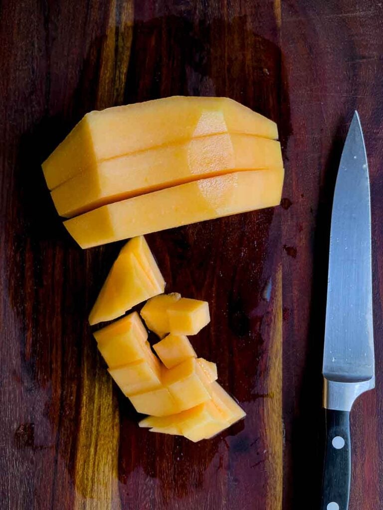 Cantaloupe cut into cubes on a dark cutting board.
