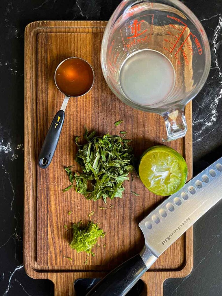 Lime juice, lime zest, honey, a fresh chopped mint on a dark cutting board.