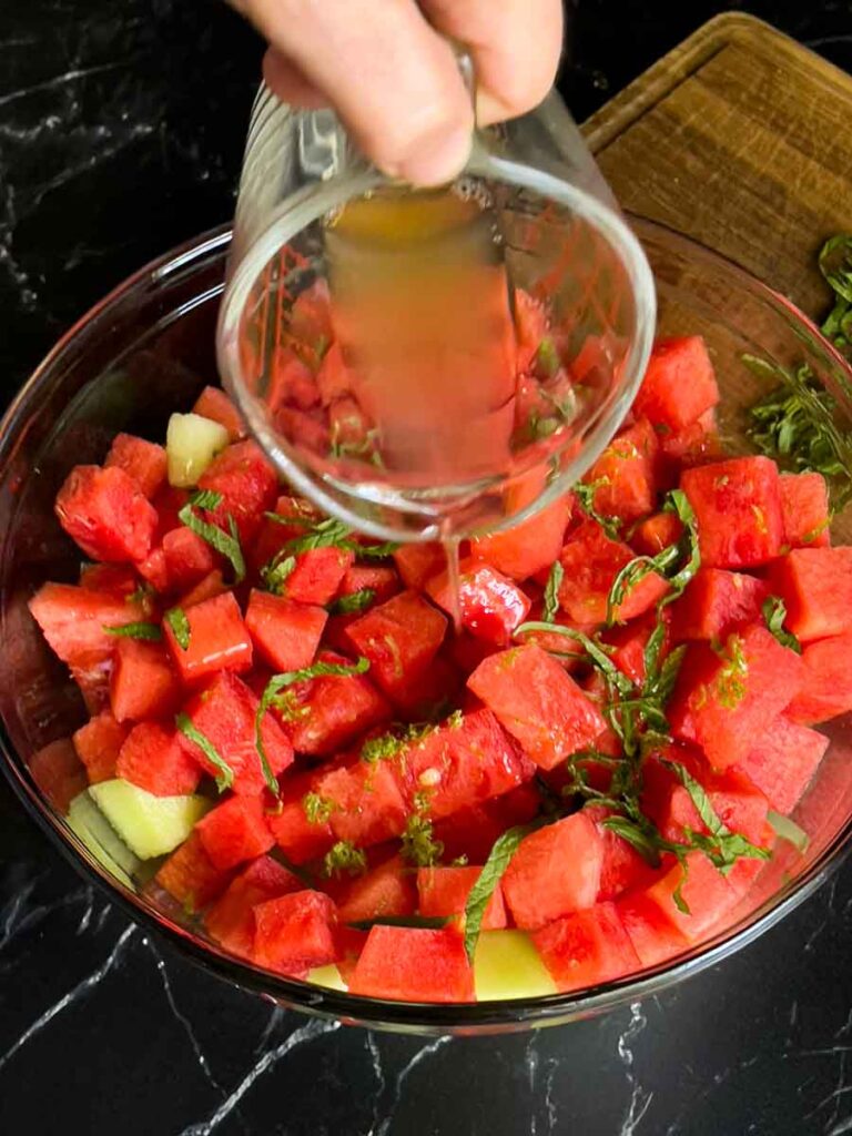 Honey lime dressing being poured over the mixed melon fruit salad.