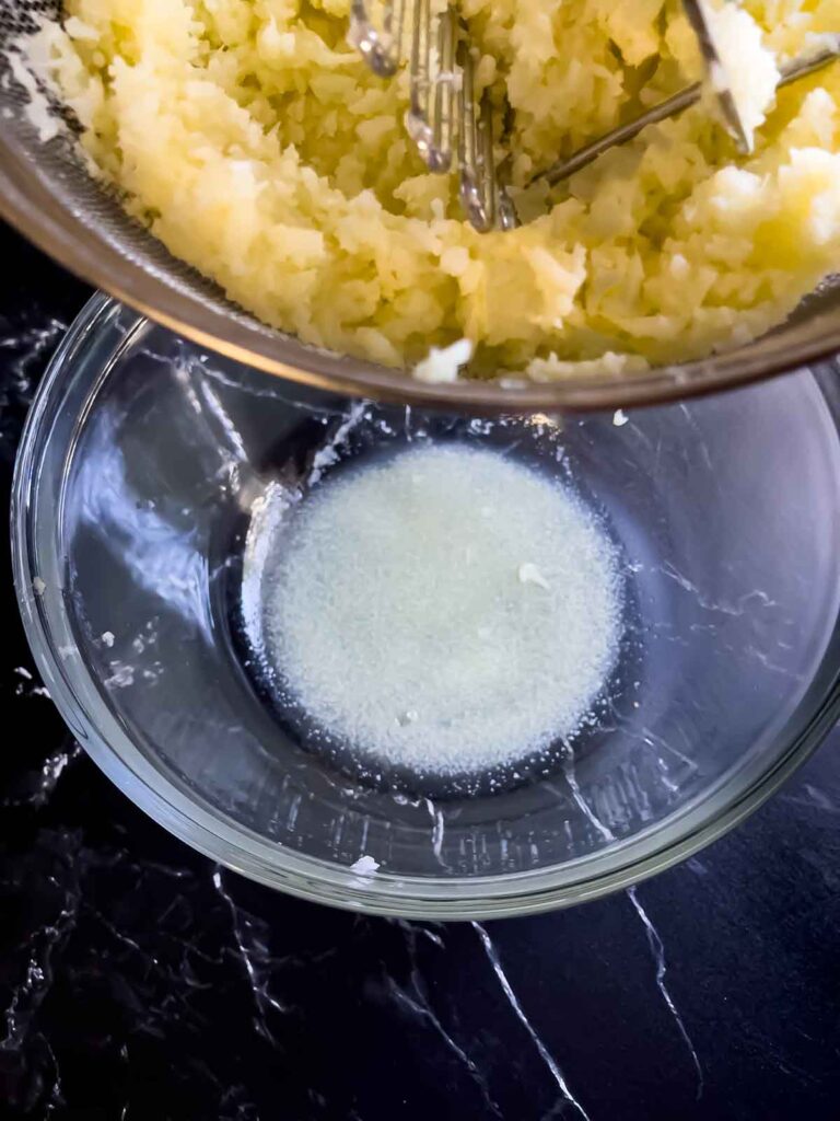 The water drained from the mashed cauliflower in the bottom of a glass bowl.