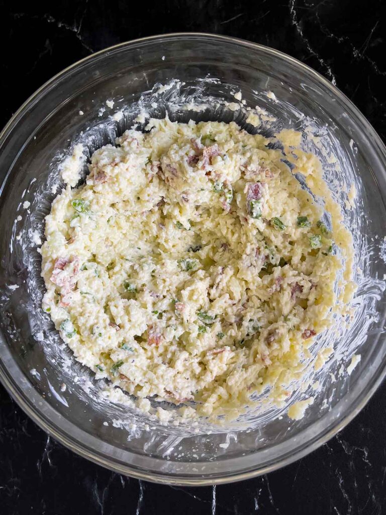 The unbaked loaded cauliflower mash casserole in a glass bowl.