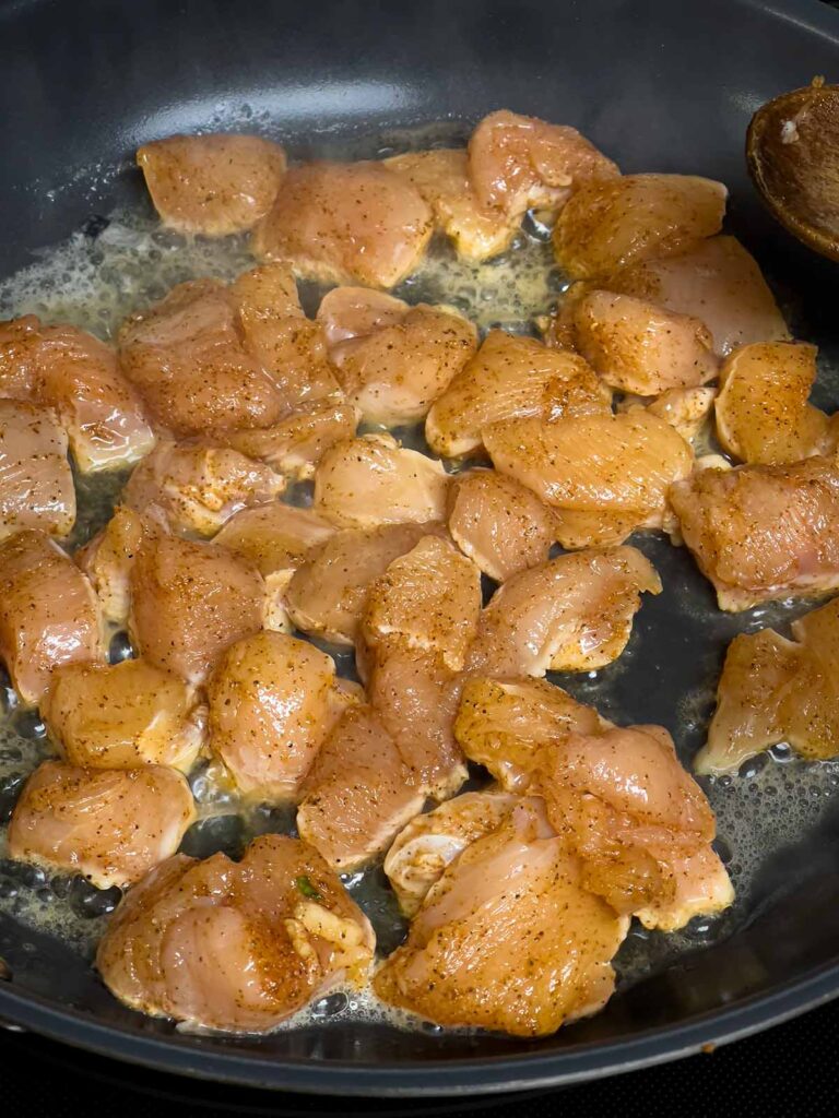 Cut up chicken breast cooking in a skillet.