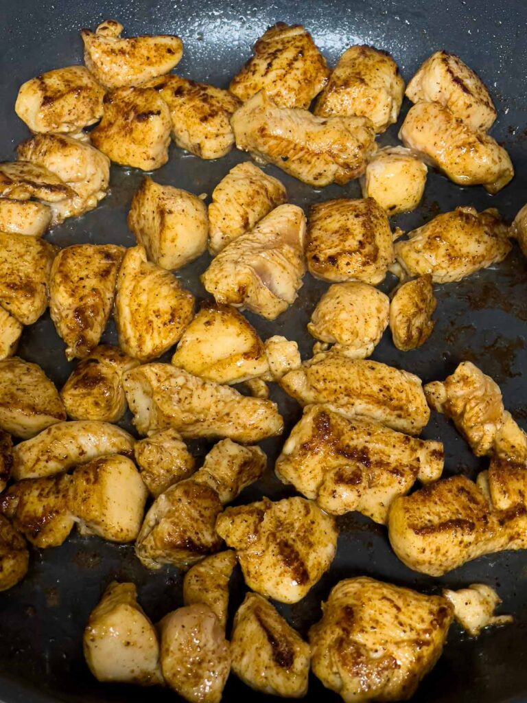 Browned cut up chicken breast in a skillet.