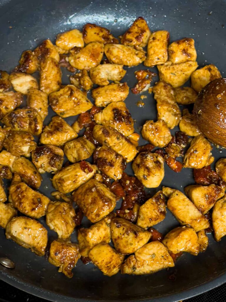 Browned chicken breast and sun dried tomatoes in a skillet.