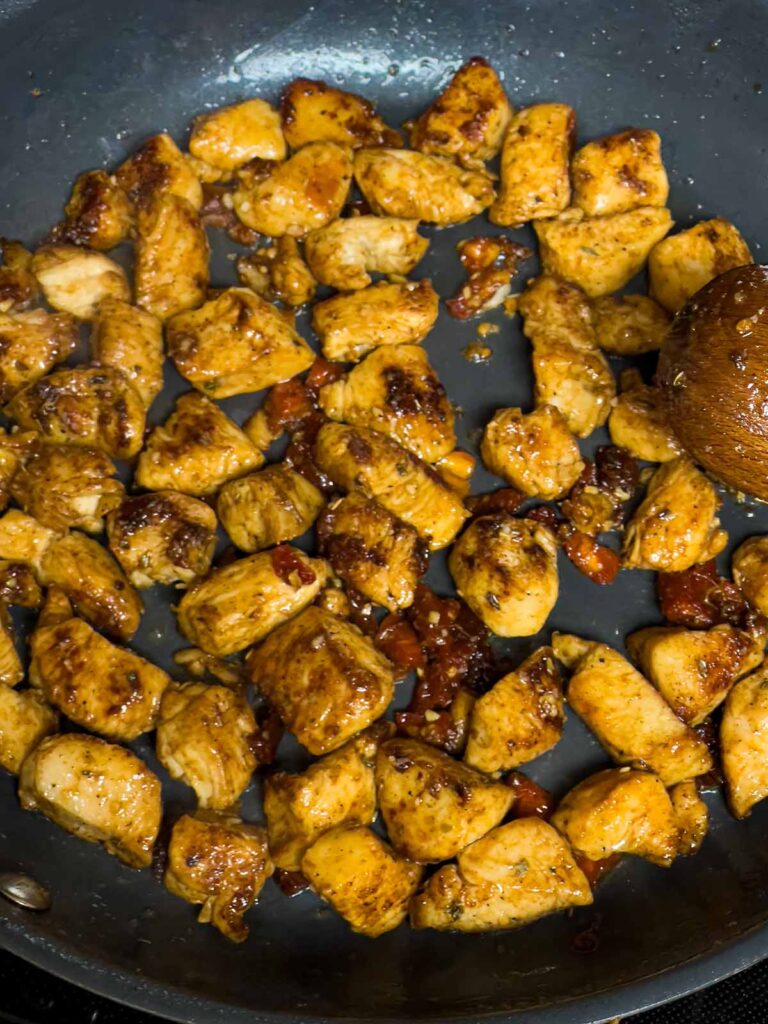 Browned chicken breast and sun dried tomatoes in a skillet.