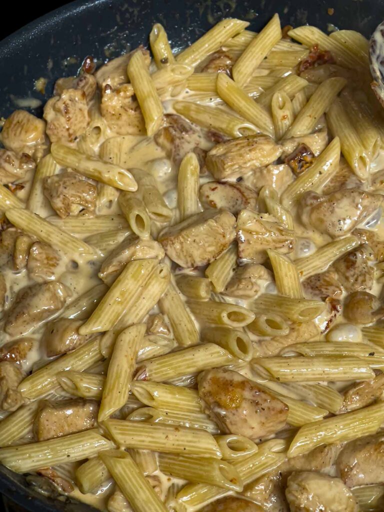 Cajun chicken pasta being combined in a skillet.