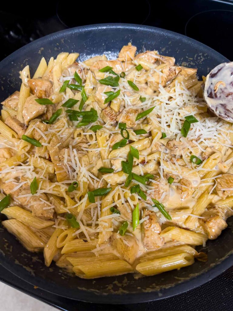 Green onions and parmesan cheese being added to cajun chicken pasta.