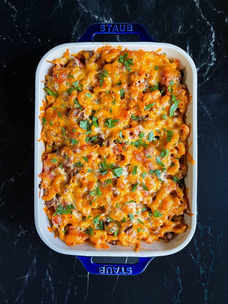 Cheesy beefaroni in a blue casserole dish garnished with chopped parsley.