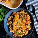 Cheesy beefaroni served in a dark bowl with the casserole off to the side.