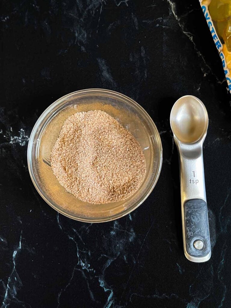 Cinnamon sugar topping for oyster cracker churro snack mix in a glass ramekin on a dark surface.