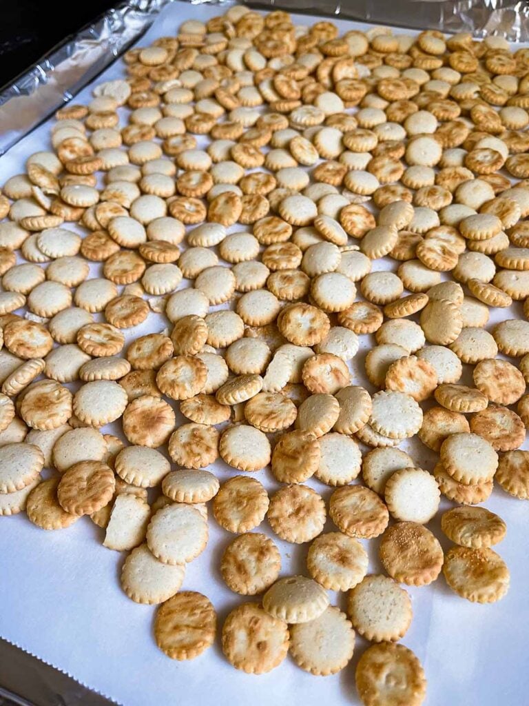 Oyster crackers spread out on a lined baking sheet.
