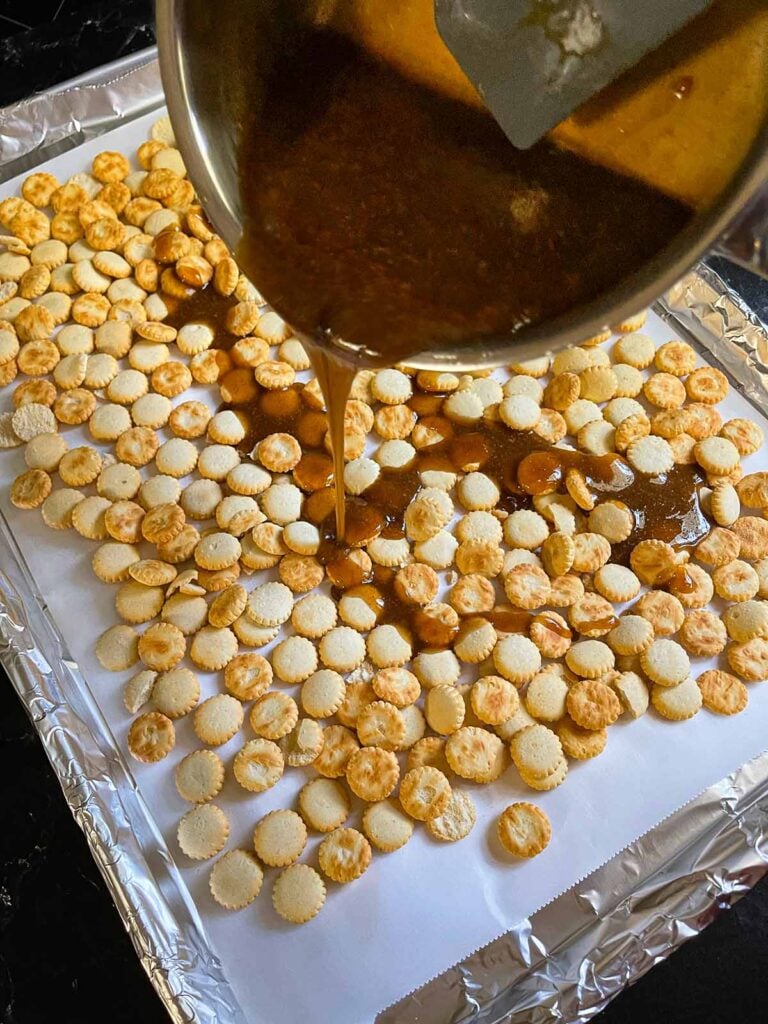 Pouring the toffee mixture over the oyster crackers in a lined baking sheet.