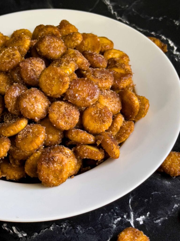 Oyster cracker churro snack mix in a light bowl on a dark surface.