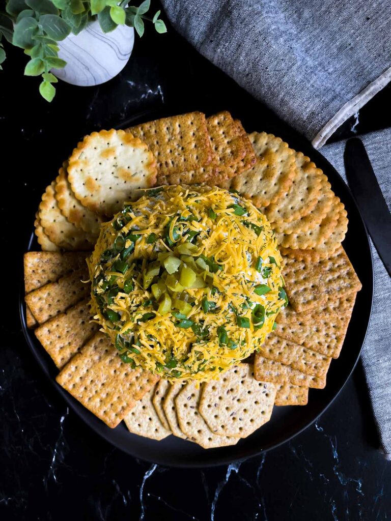 Dill pickle cheese ball on a dark plate on a dark surface with grey napkins.