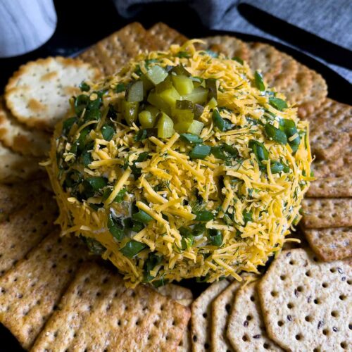 Dill pickle cheese ball on a dark plate on a dark surface with grey napkins.