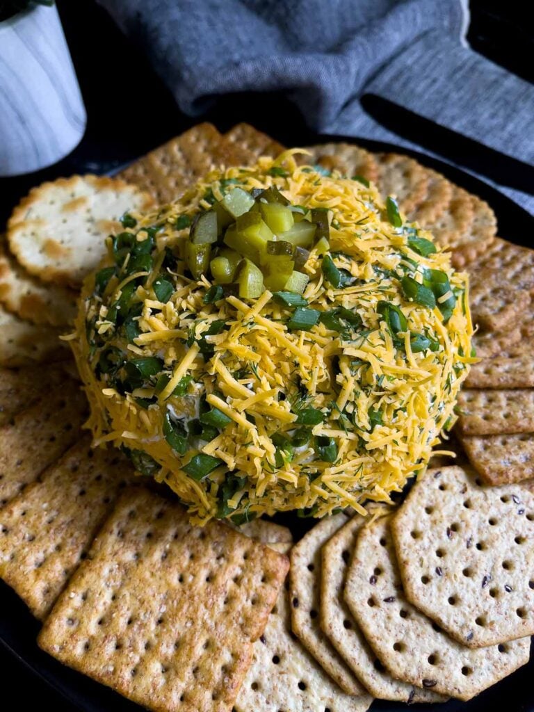 Dill pickle cheese ball on a dark plate on a dark surface with grey napkins.