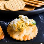 Dill pickle cheese ball scooped on a cracker on a dark surface.