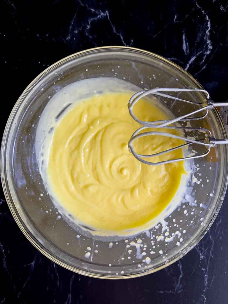 Pudding and milk mixture in a glass mixing bowl for the lemon icebox cake on a dark surface.